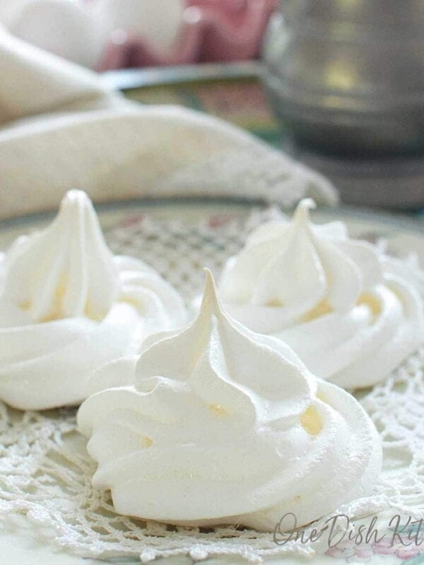three meringue cookies on a doily on top of a white plate next to a beige napkin and eggs.