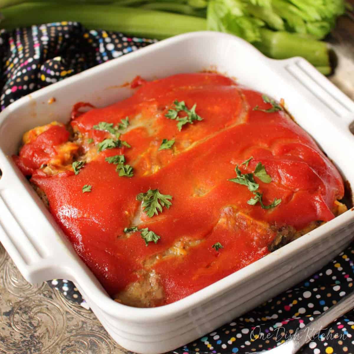 a small bacon cheeseburger meatloaf topped with ketchup glaze topped with chopped parsley in a small baking dish.