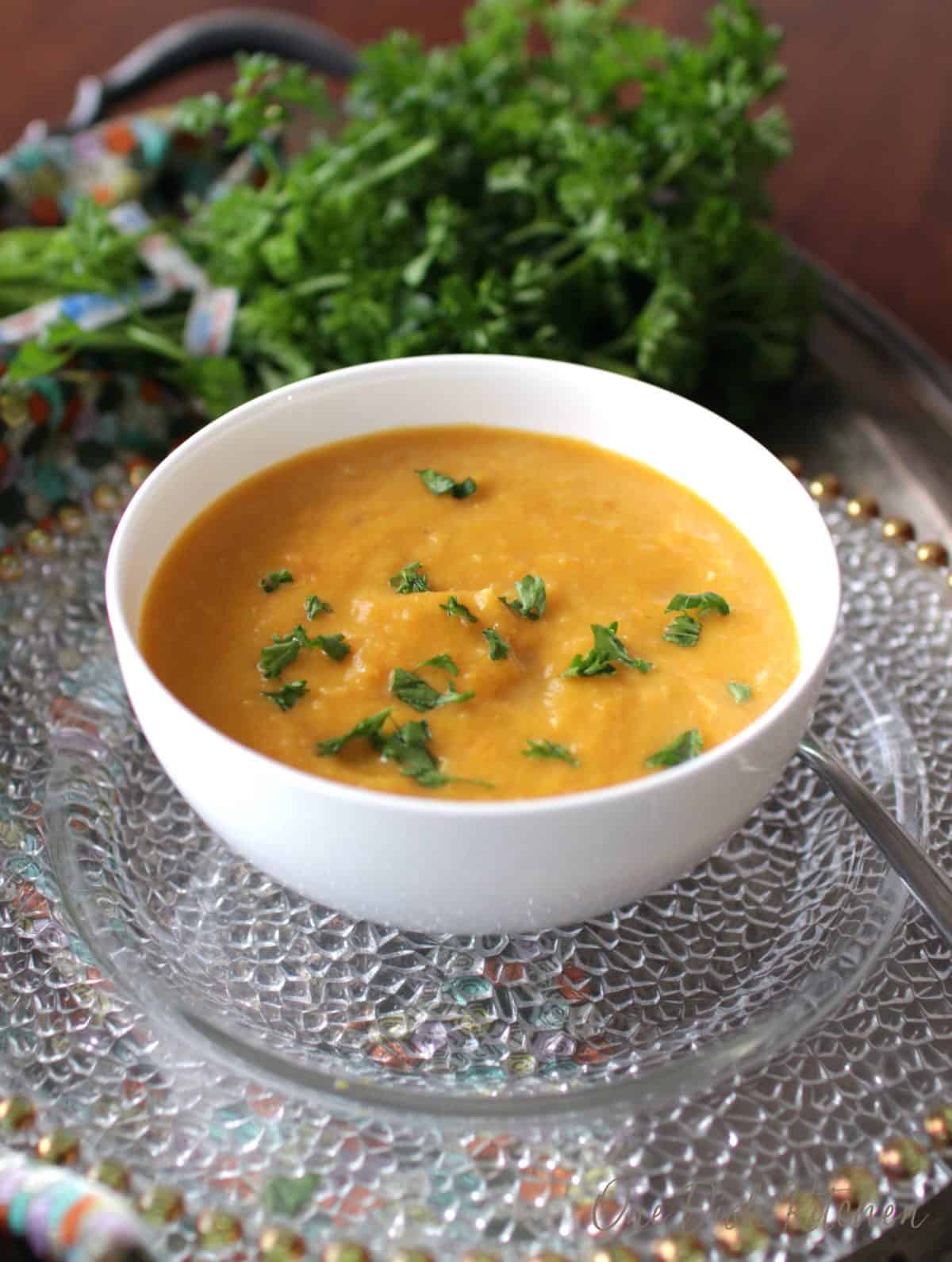 a white bowl filled with butternut squash soup next to a big bunch of parsley.