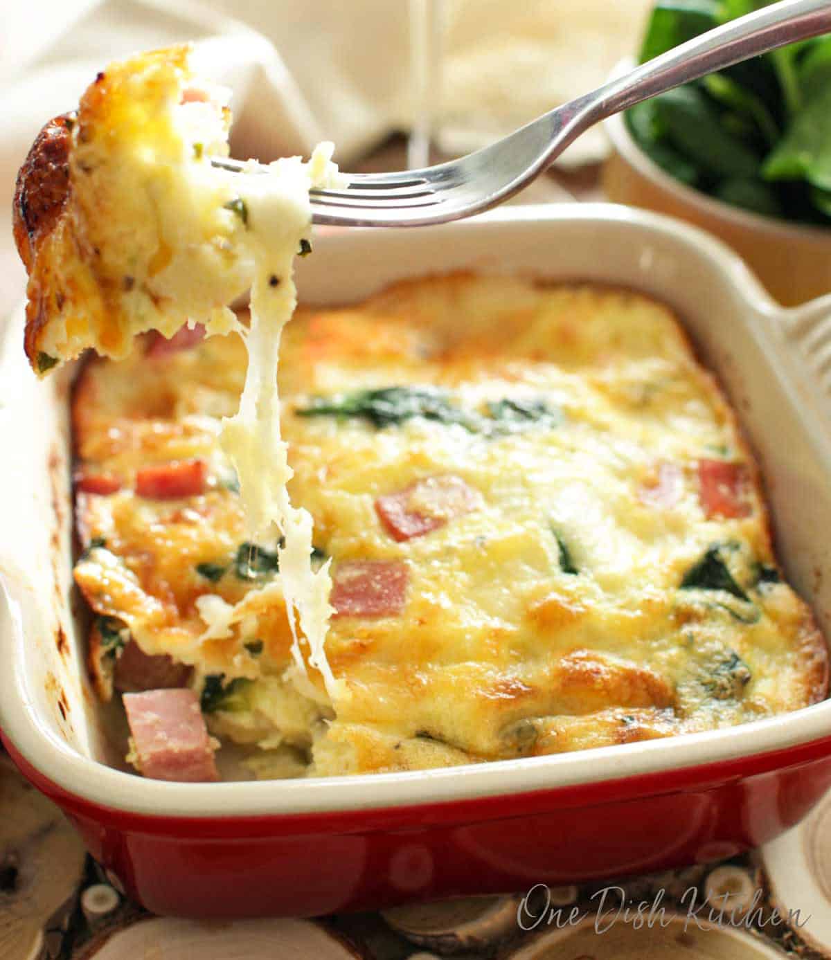 Cheese hanging off a fork in a spinach quiche with a glass of red wine in the background.