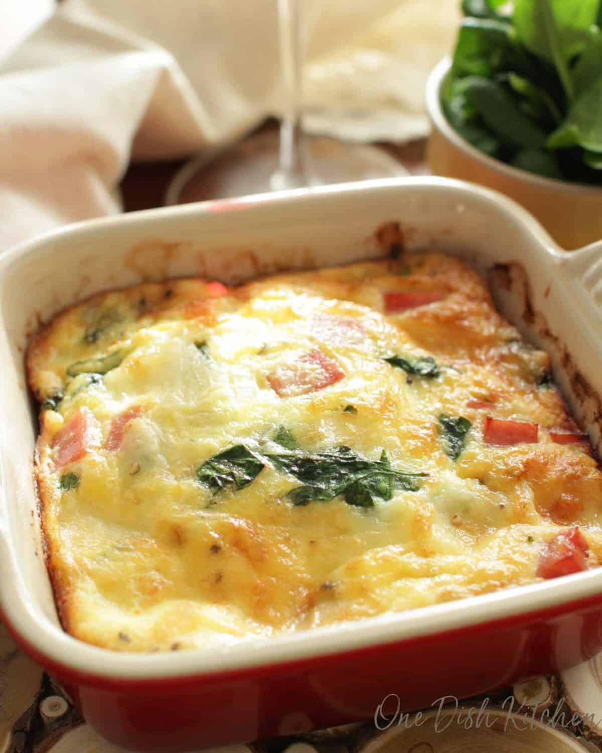 A spinach quiche in a small baking dish next to a glass of red wine.