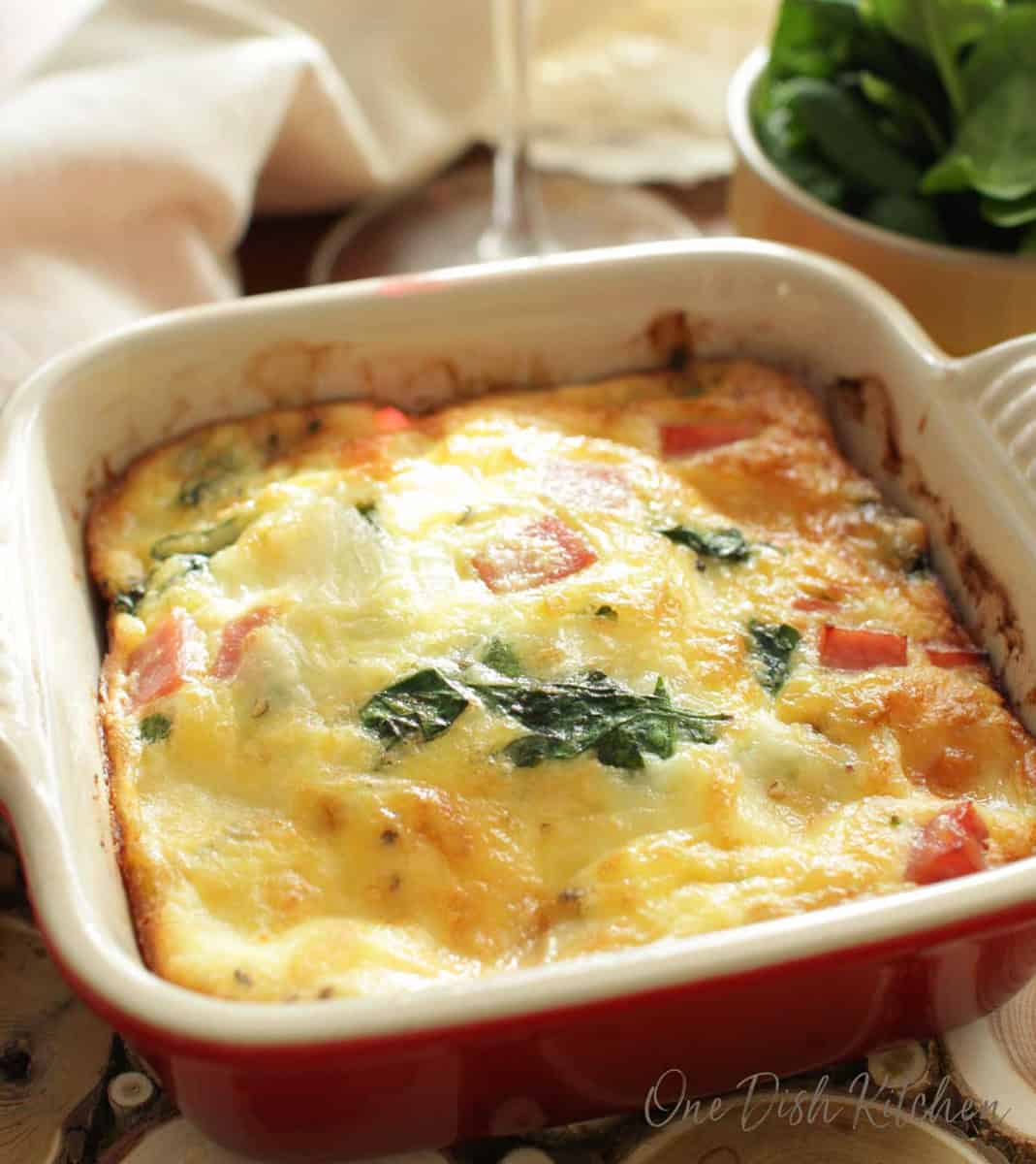 A spinach quiche in a small baking dish next to a glass of red wine.