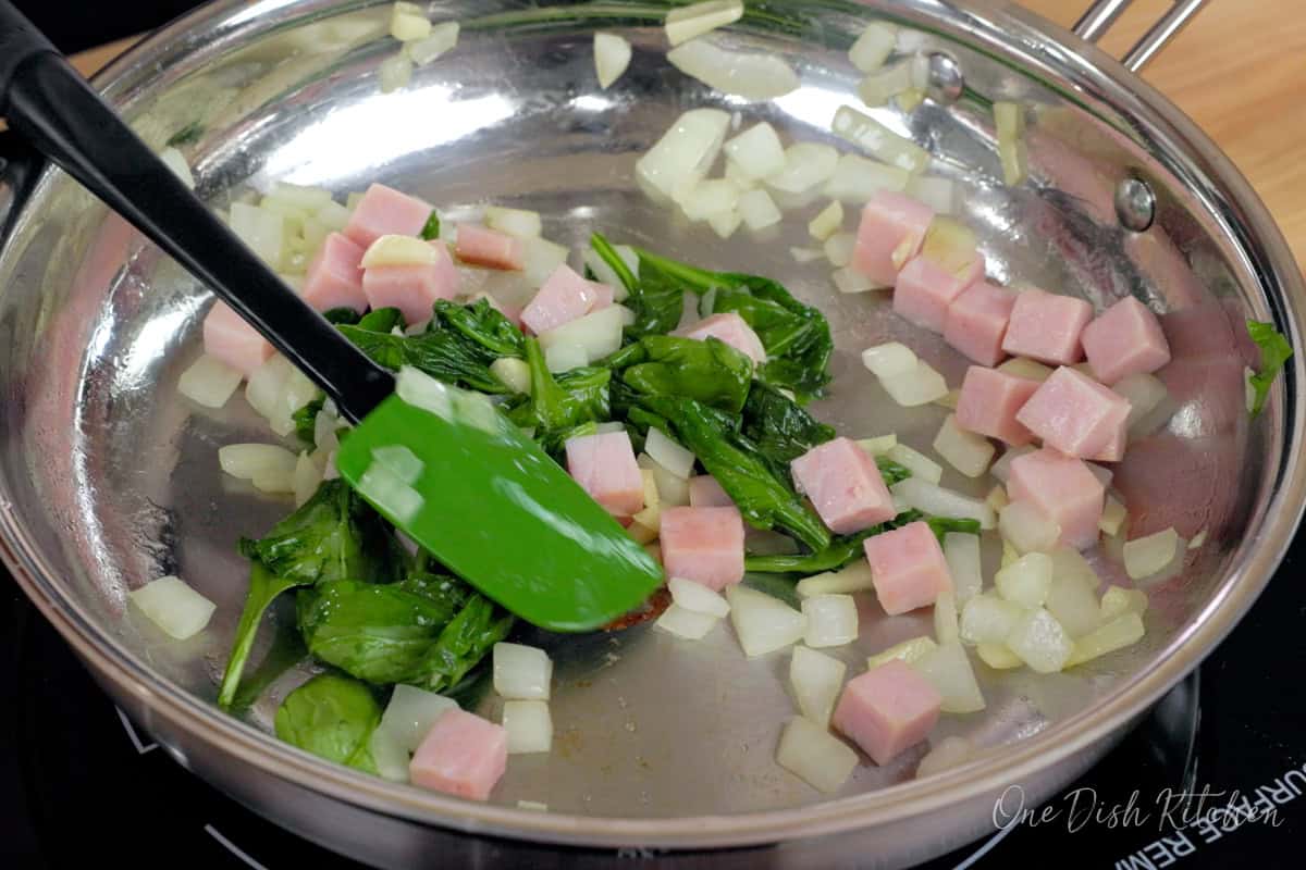 spinach wilting in a skillet with ham.