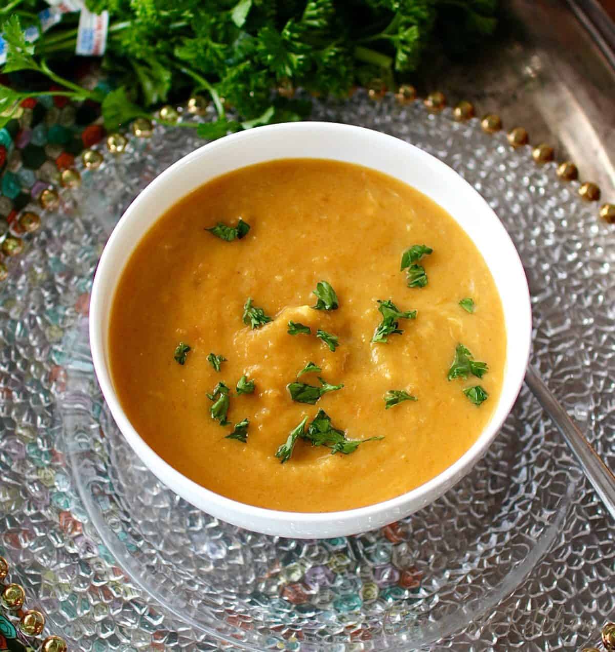 an overnight picture of a bowl of golden colored butternut squash soup topped with chopped parsley.