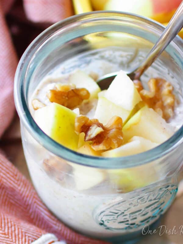 a jar of overnight oats with rolled oats, yogurt, milk, apples, nuts and honey.