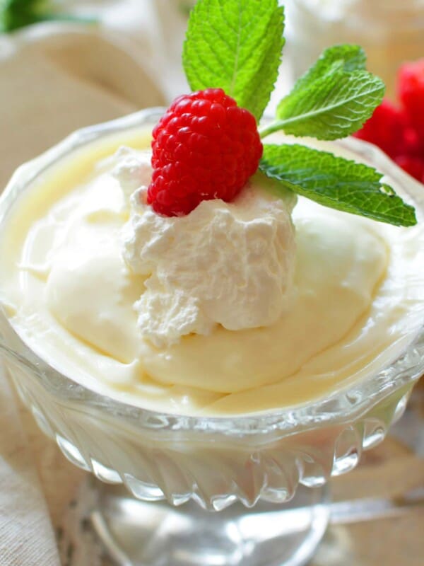 homemade vanilla pudding in a dessert bowl topped with whipped cream, berries, and fresh mint