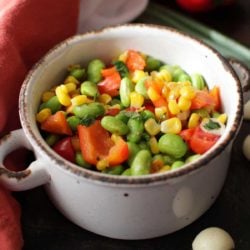 an edamame salad with corn and peppers in a bowl next to an orange napkin