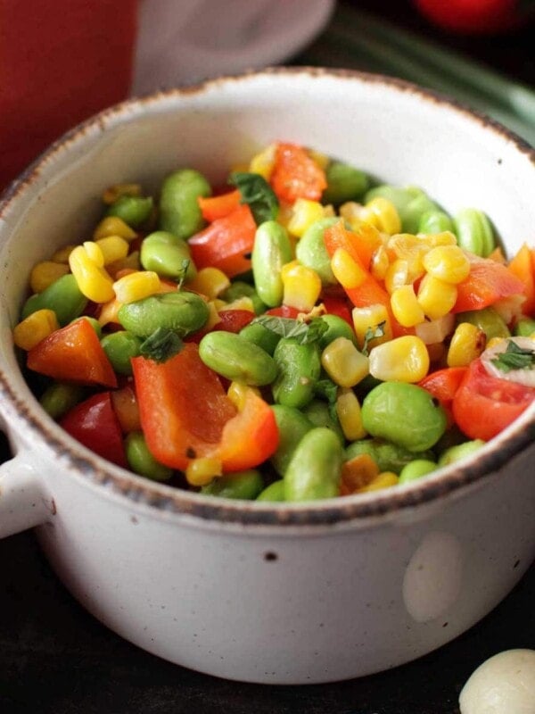 an edamame salad with corn and peppers in a bowl next to an orange napkin