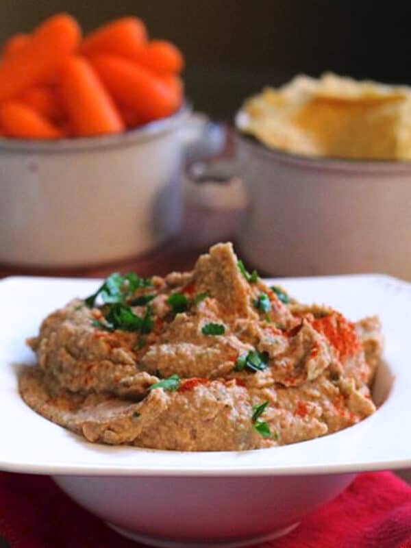 black eyed pea hummus in a white bowl next to a bowl of carrots.