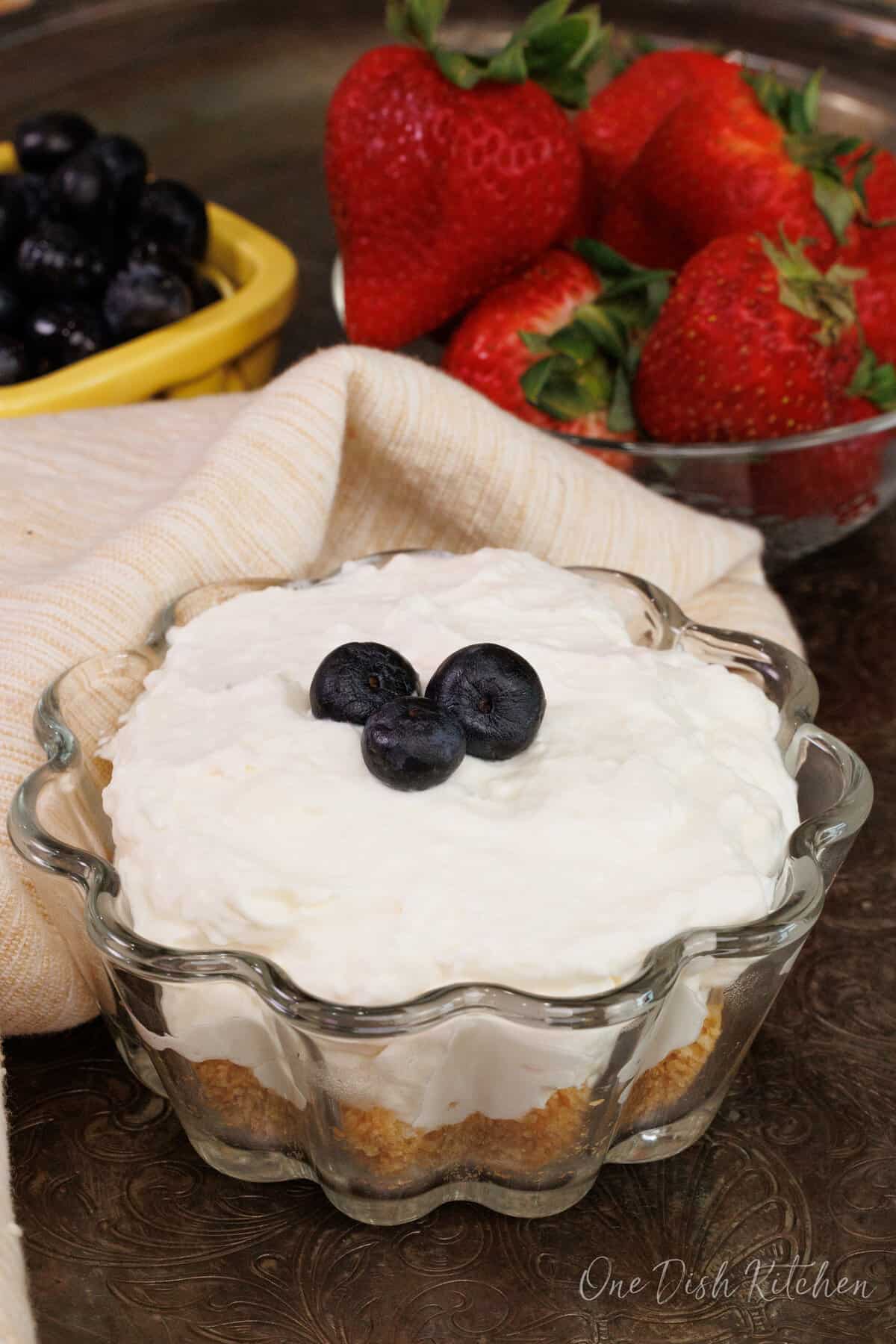 a small cheesecake in a dessert dish next to a bowl of strawberries.