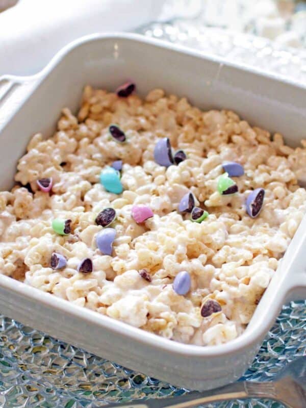 a white square dish holding a single rice krispie treat topped with crushed chocolate candies.