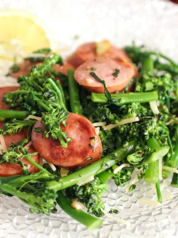 sauteed broccolini with sausage on a plate next to a slice of lemon.
