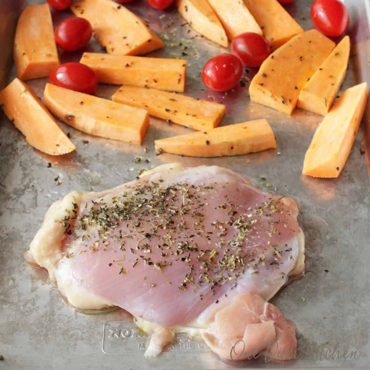 one chicken thigh and sliced vegetables on a sheet pan.