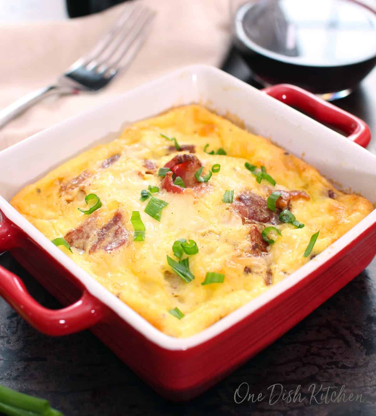 a small crustless quiche lorraine for one person on a silver tray next to a glass of wine.
