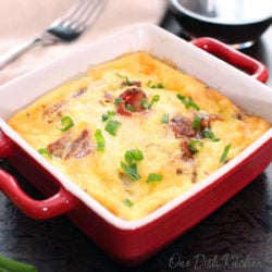 a mini quiche lorraine in a small red baking dish next to a glass of red wine