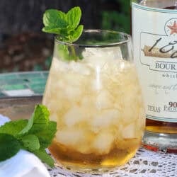 a single serving mint julep in a glass next to fresh mint and a bottle of bourbon.