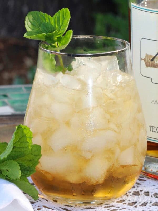 a single serving mint julep in a glass next to fresh mint and a bottle of bourbon.