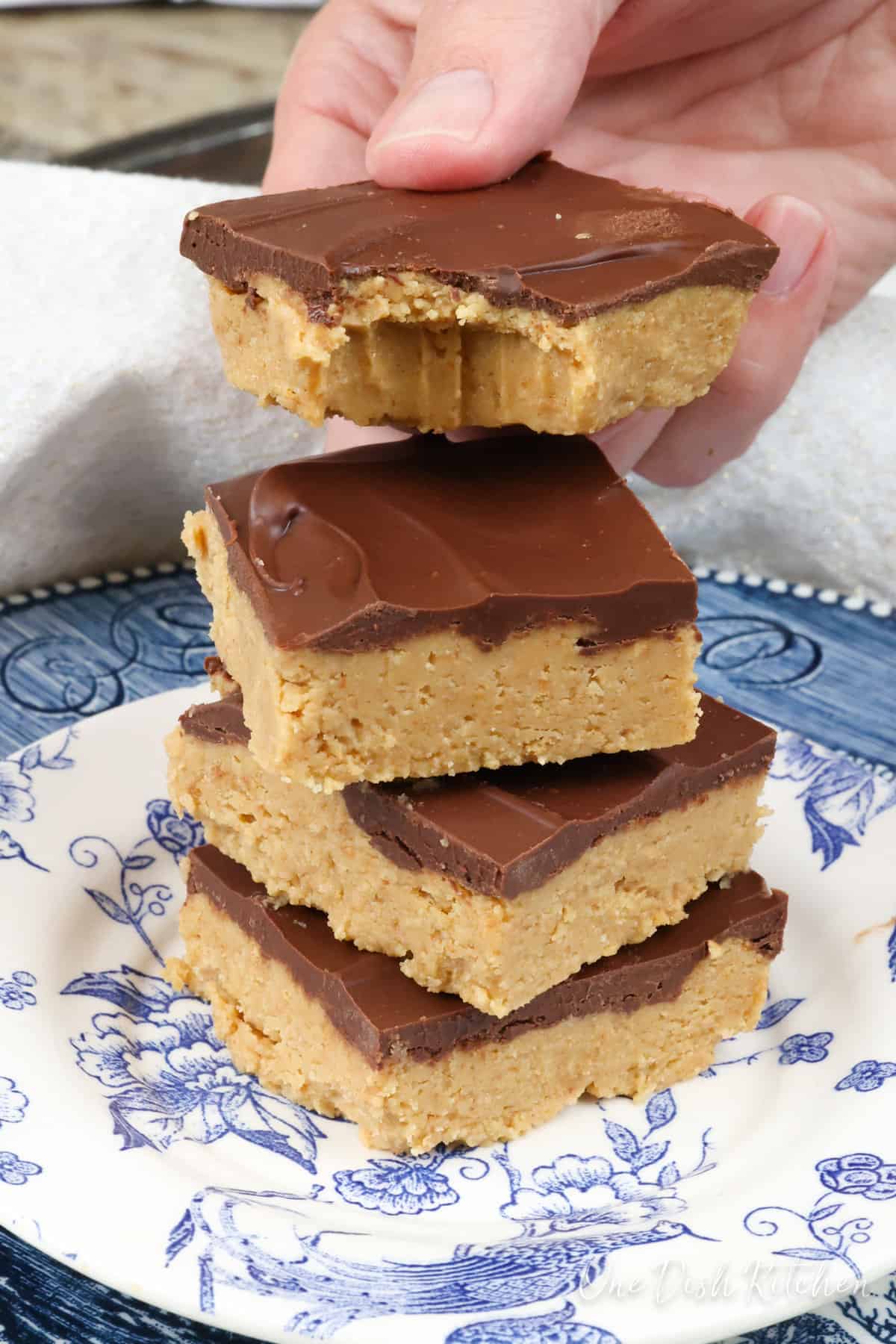 four peanut butter chocolate bars on a plate with a bite taken out of one.