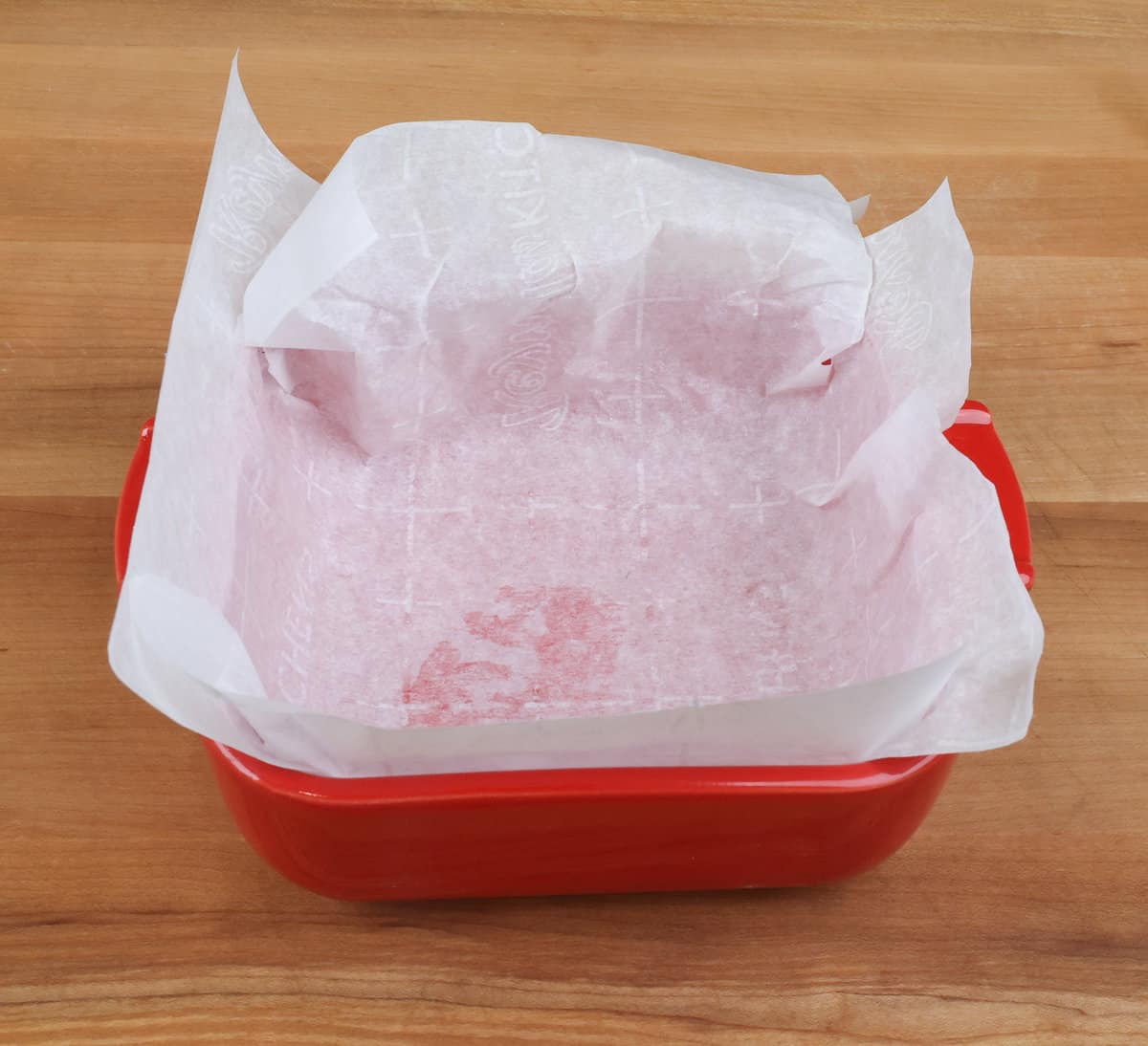 a square red baking dish lined with parchment paper.