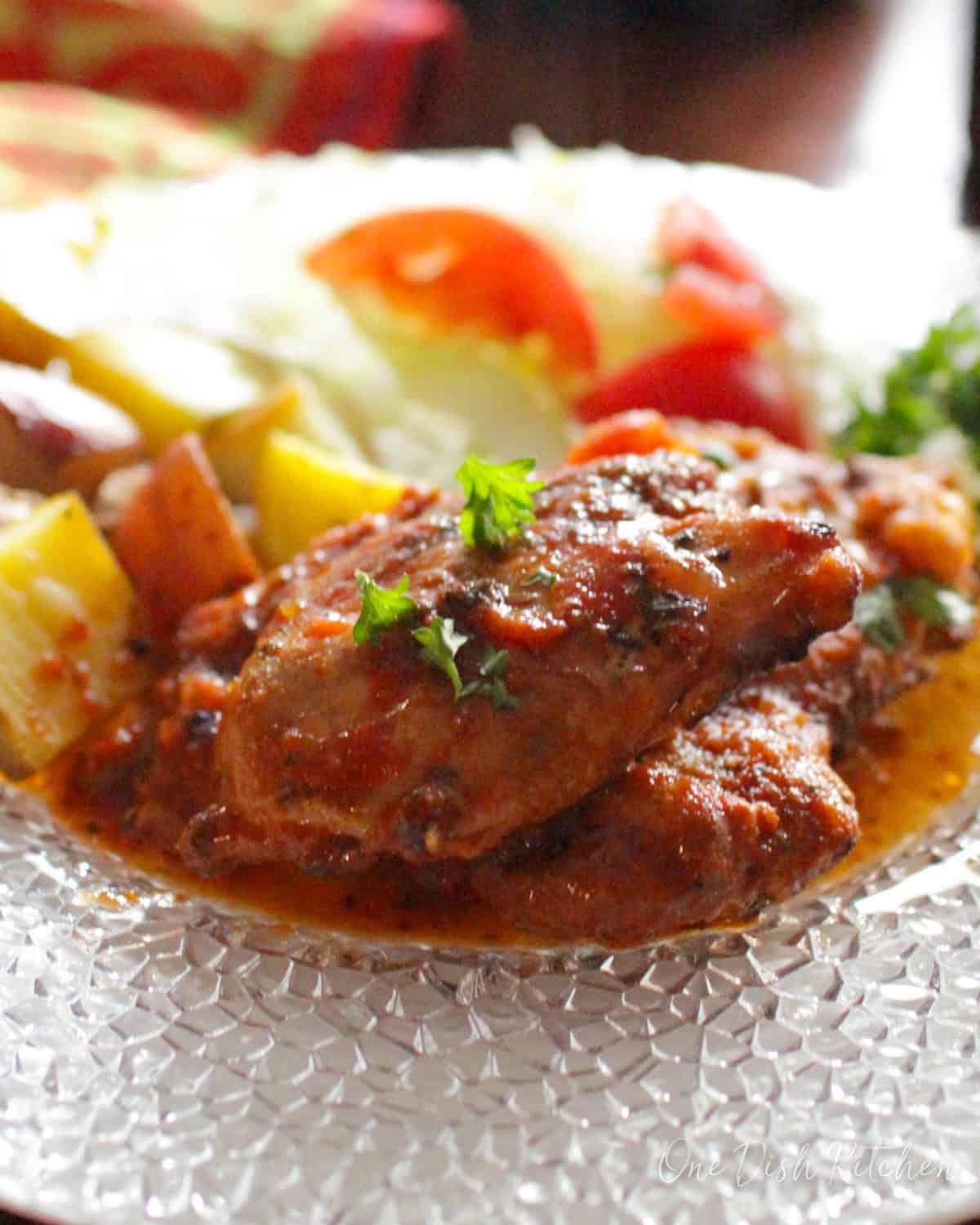 slow cooker italian chicken on a plate next to roasted potatoes.