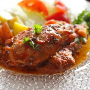 italian chicken on a plate next to potatoes and a salad.