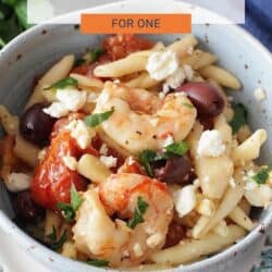 a bowl of pasta filled with shrimp , olives and roasted tomatoes.