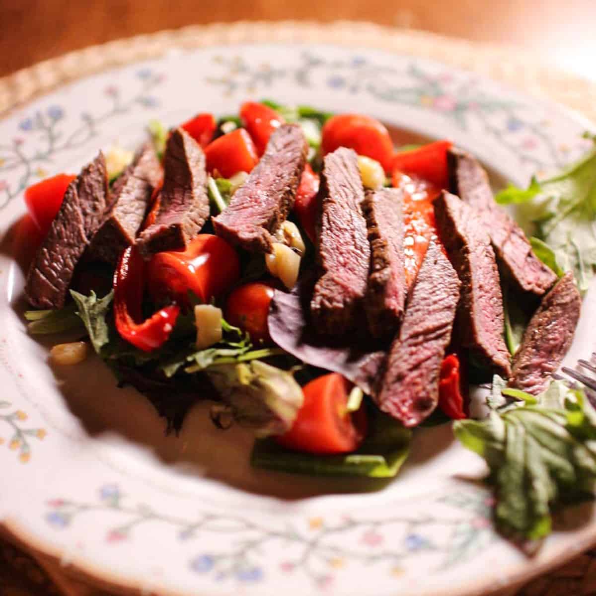 a small salad topped with strips of steak.