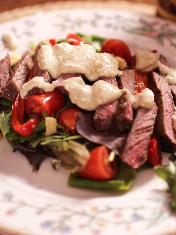 a steak salad on a plate topped with Gorgonzola dressing.