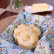 three drop biscuits on a blue napkin next to a plate of butter.
