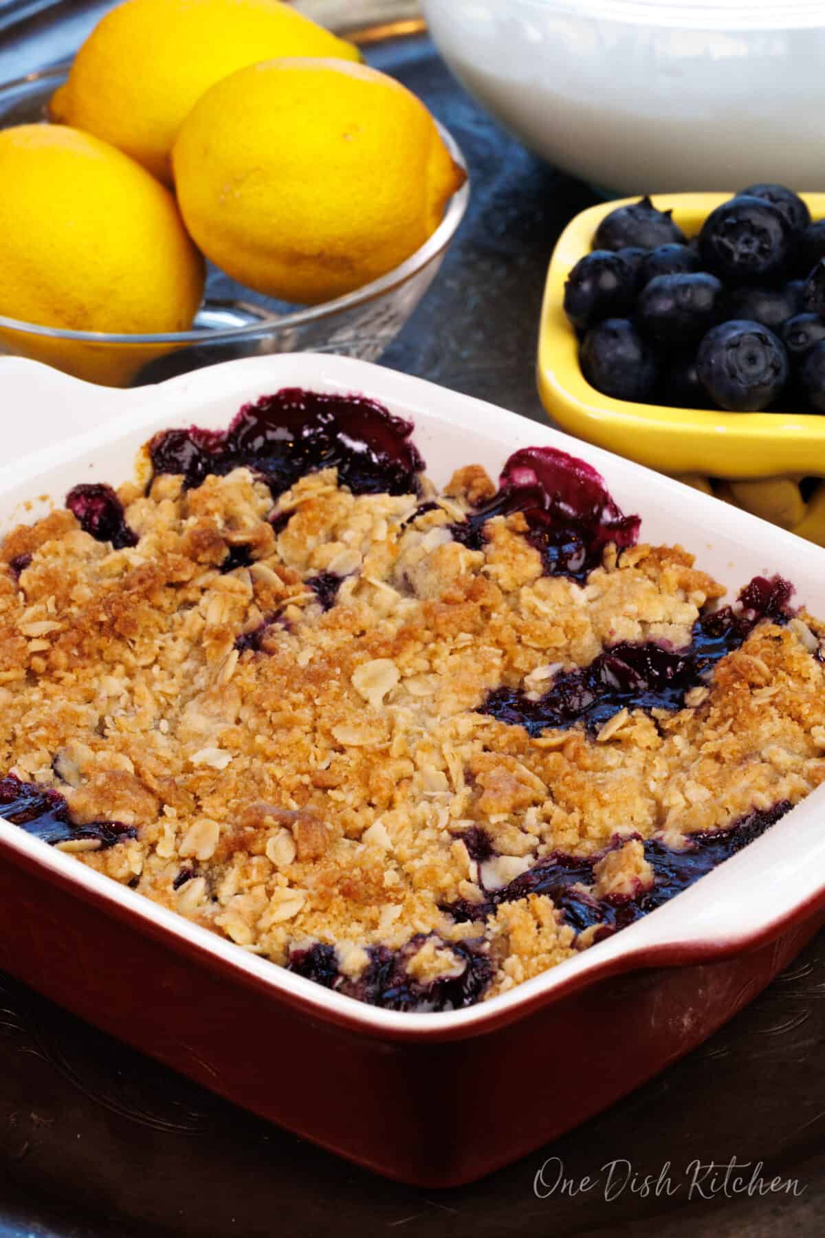 a blueberry crumble in a rectangular baking dish next to a bowl of blueberries