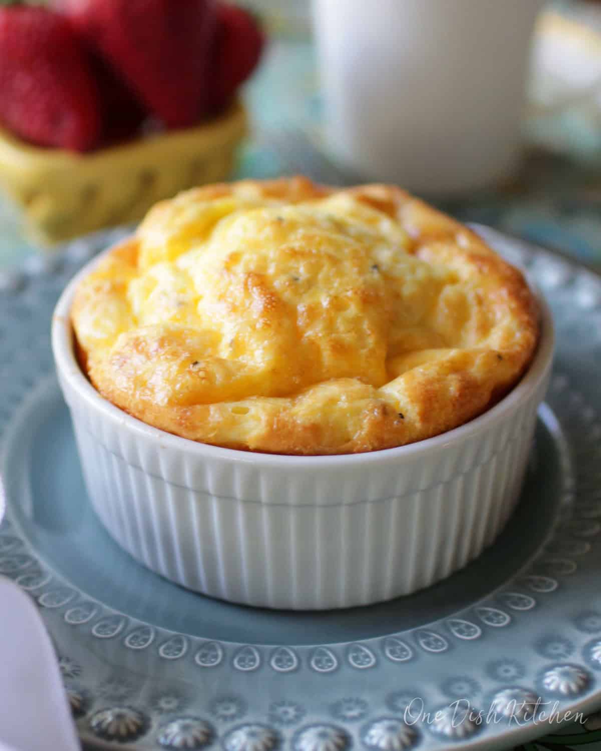 Baked eggs in a small ramekin next to a small bowl of strawberries and a coffee mug all on a metal tray.