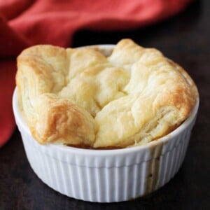 a mini chicken pot pie in a white ramekin topped with puff pastry.