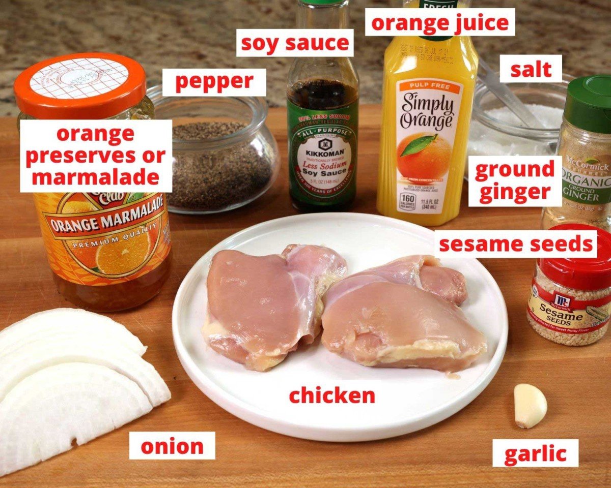 two chicken thighs, orange marmalade, orange juice, soy sauce, and other ingredients needed to make orange chicken on a wooden cutting board.
