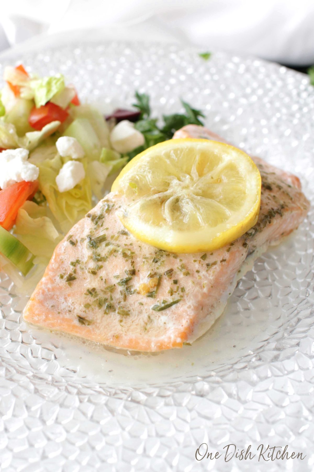 a piece of salmon that was baked in foil on a white plate topped with a lemon slice next to a salad.
