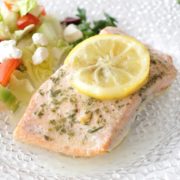 baked salmon on a white plate next to lettuce and tomatoes
