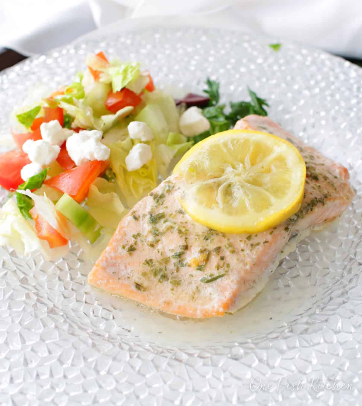 baked salmon on a plate topped with lemon slices and next to a salad.