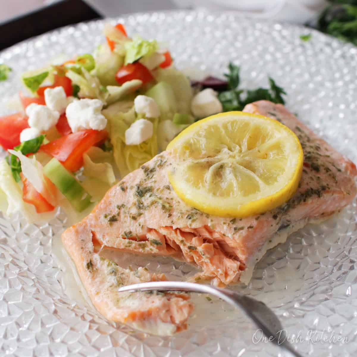 baked salmon on a plate topped with a lemon slice and salad.