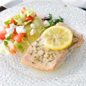 baked salmon on a plate topped with lemon slices and next to a salad.