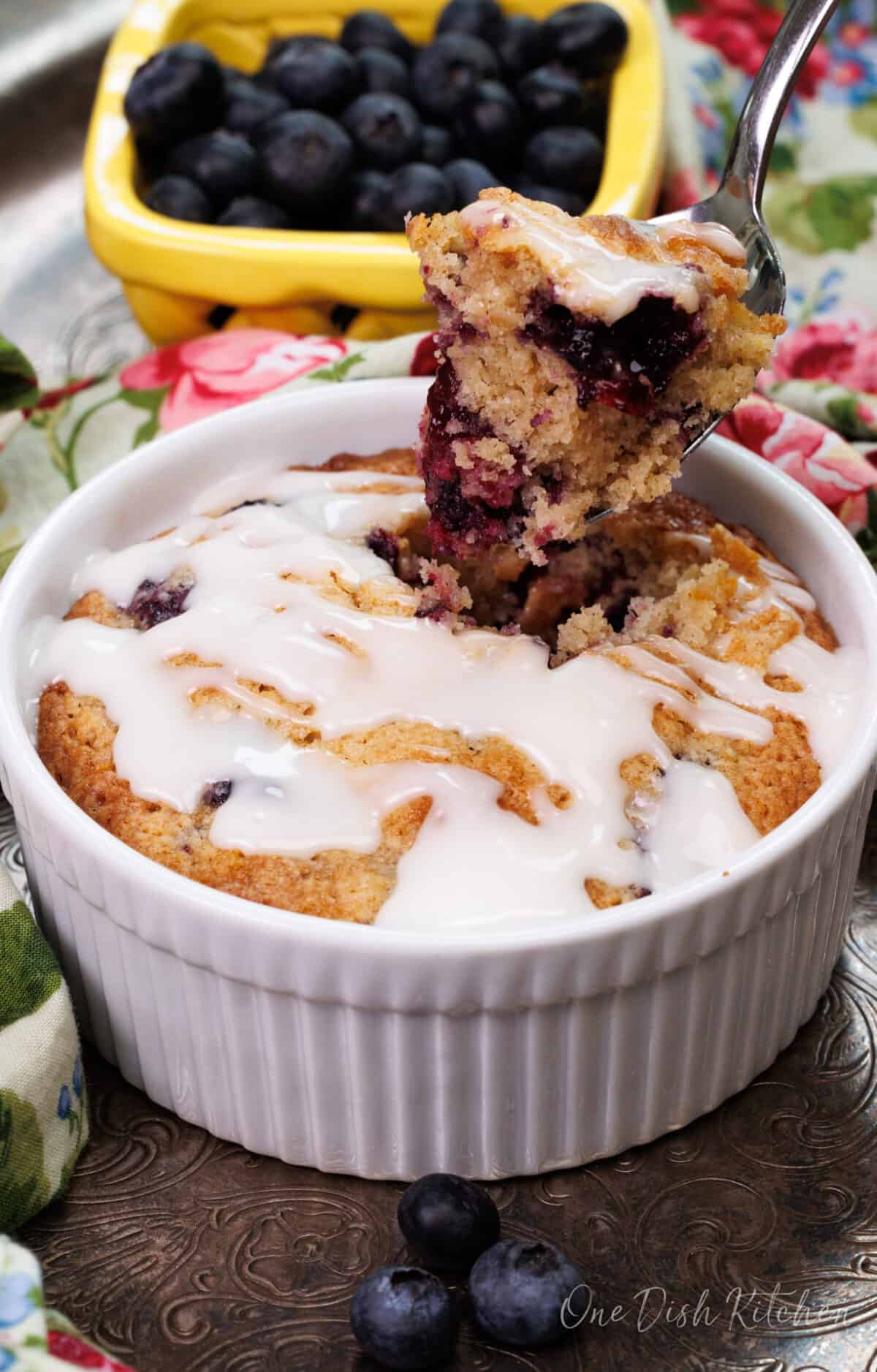 a small blueberry coffee cake in a white ramekin with a spoon on the side of the dish
