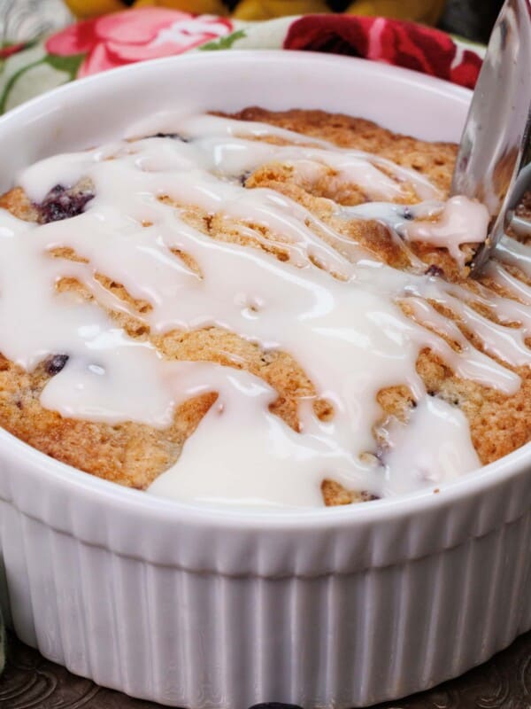 blueberry coffee cake with a glaze on a silver tray next to a floral napkin