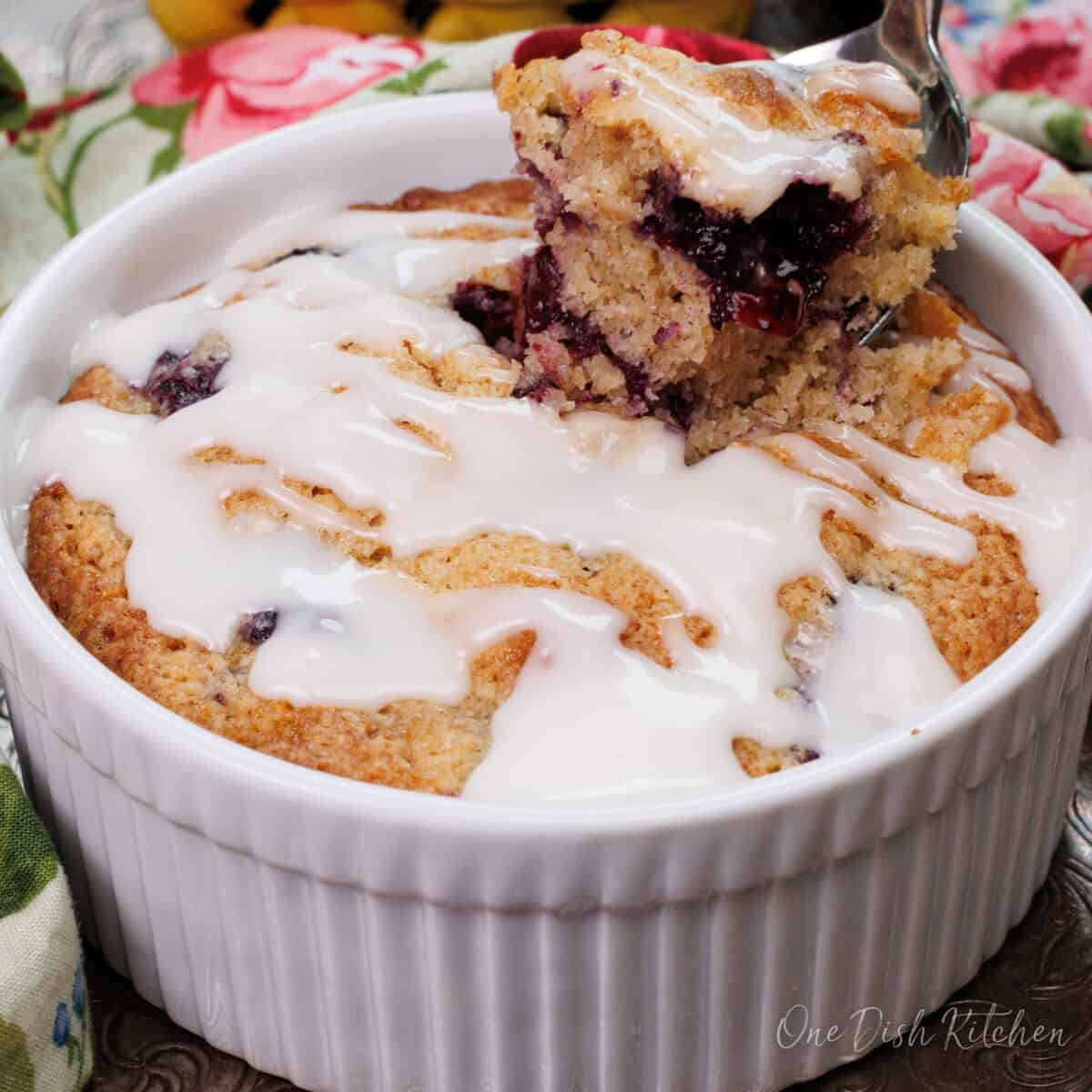 blueberry coffee cake with a glaze on a silver tray next to a floral napkin
