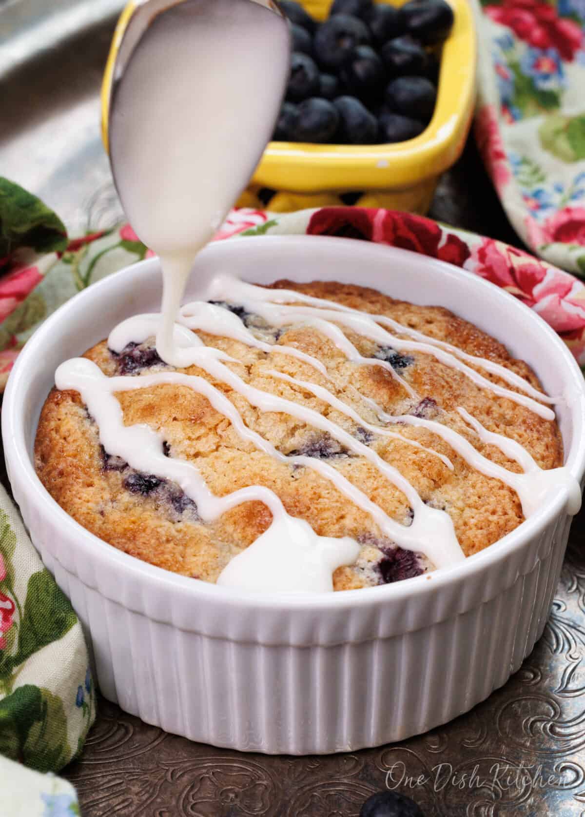 a sugar glaze drizzled from a spoon over a blueberry coffee cake