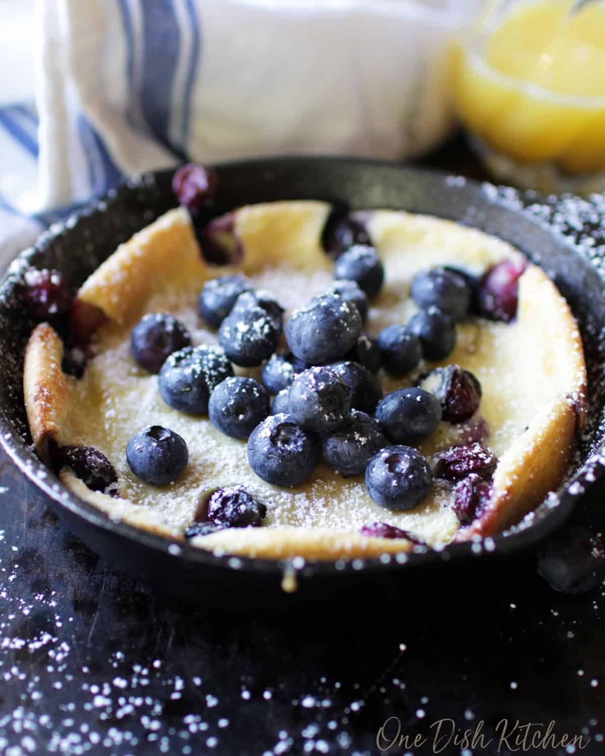A dutch baby pancake topped with blueberries and powdered sugar in a small cast iron skillet.