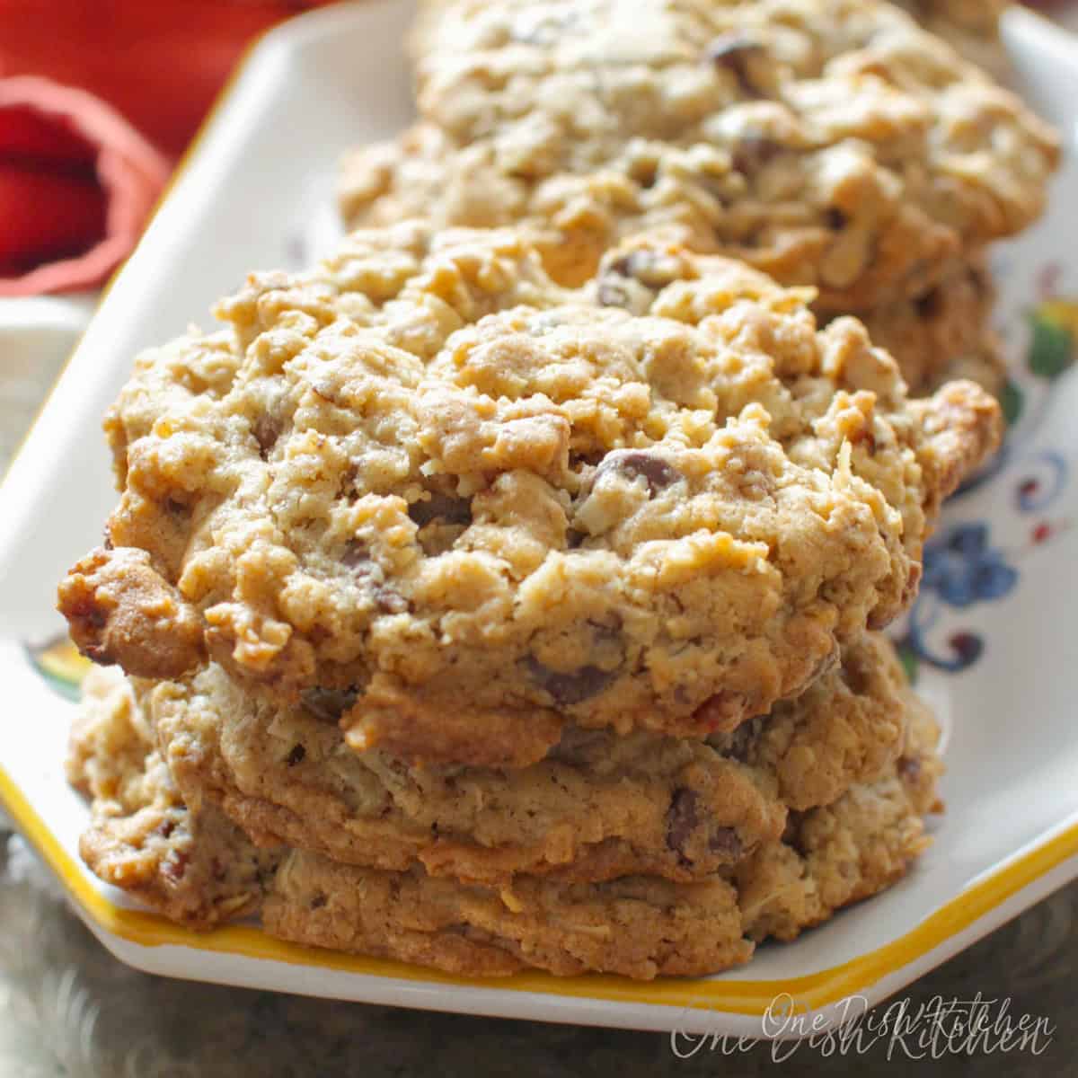 A stack of cowboy cookies on a plate next to an orange napkin.