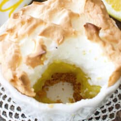 a partially eaten small lemon meringue pie on a silver tray next to a lemon