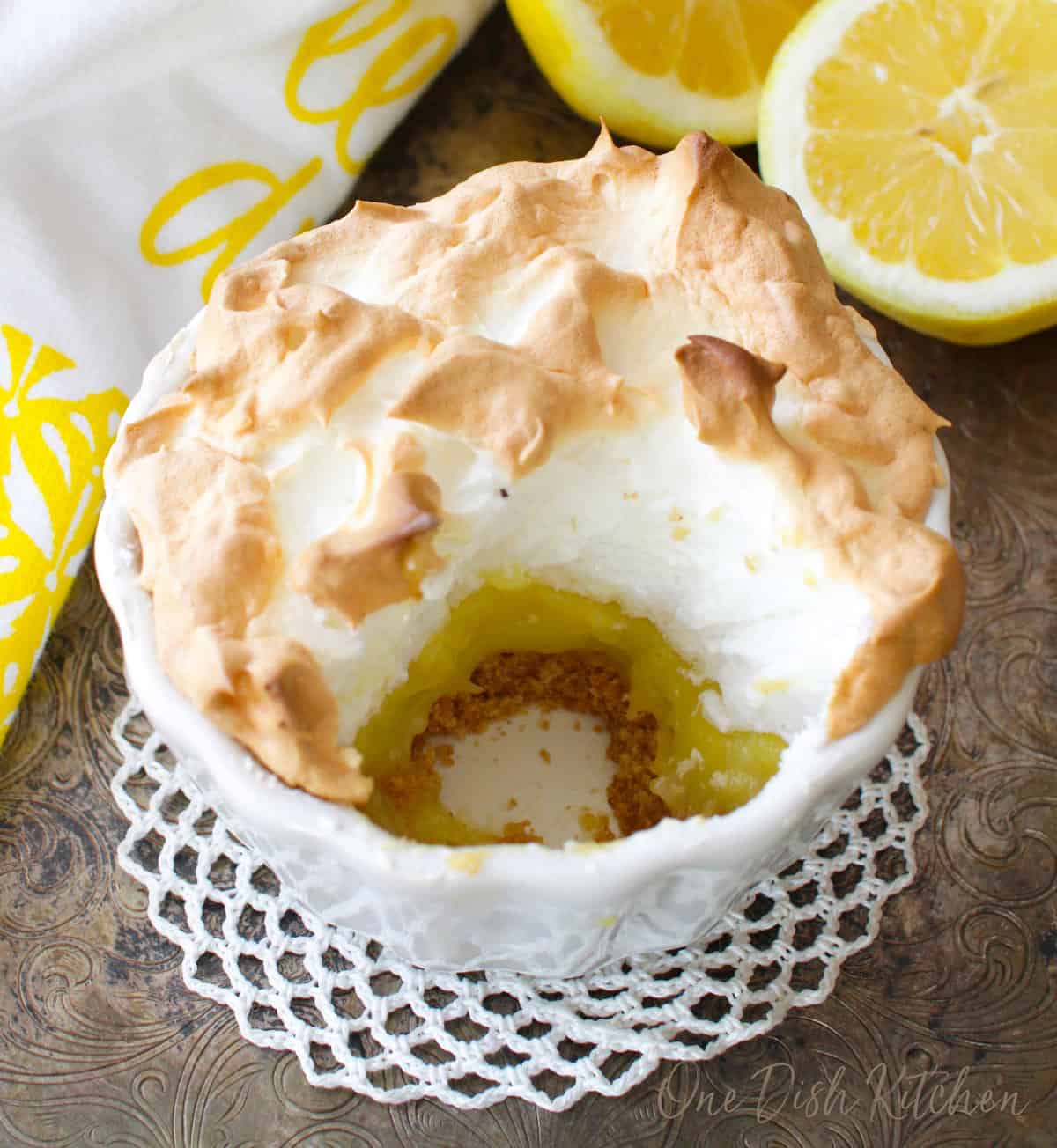 a partially eaten small lemon meringue pie on a silver tray next to a lemon.