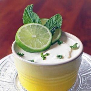 lime posset in a yellow and white ramekin topped with a slice of lime and mint leaves.