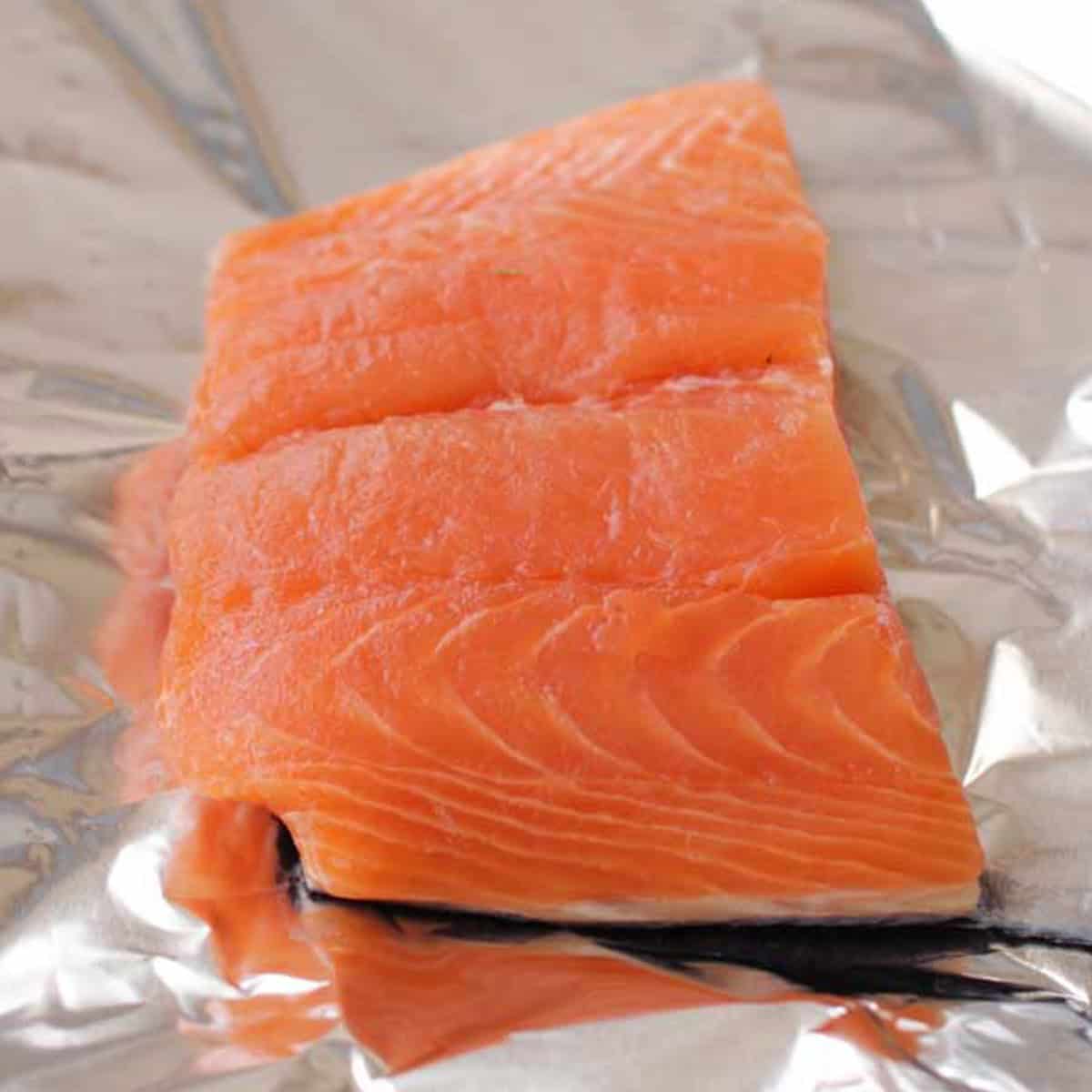 Placing a raw 6-ounce salmon fillet in the center of a large sheet of aluminum foil for baking.