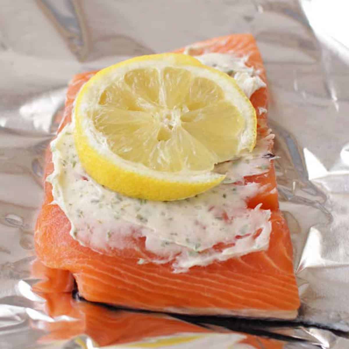 a salmon fillet on a sheet of foil topped with butter, tarragon, and a lemon slice.