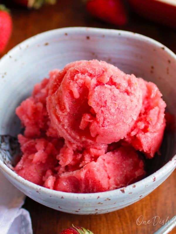 a blue bowl filled with watermelon sorbet surrounded by fresh strawberries on a wooden table.